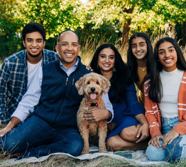 Family of five smiling in a park with their dog