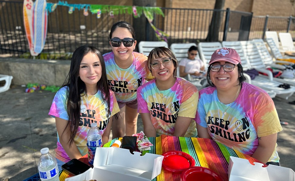 Four women in matching tie dye shirts volunteering at a community event