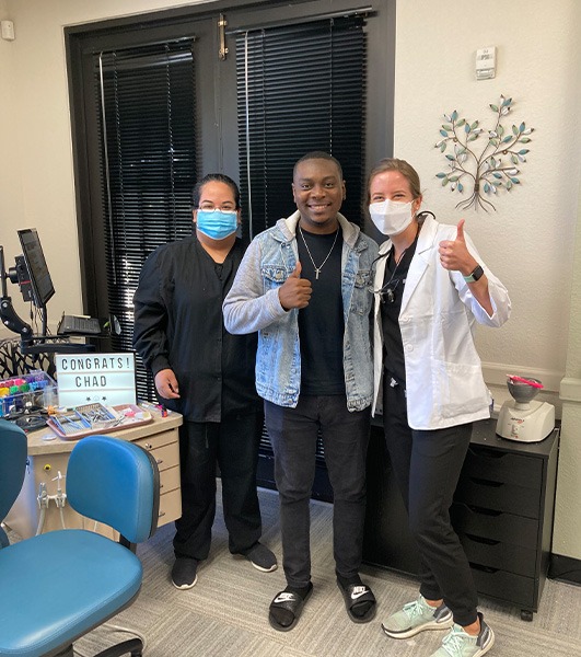 Two women giving a thumbs up while smiling with a man