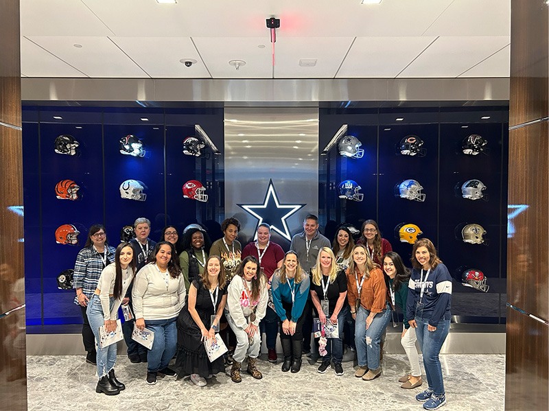 Orthodontic team smiling in front of a display case full of Dallas Cowboys football helmets