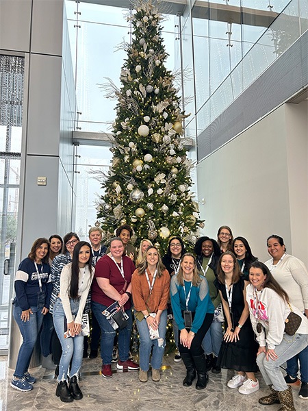 Team smiling in front of extremely tall Christmas tree