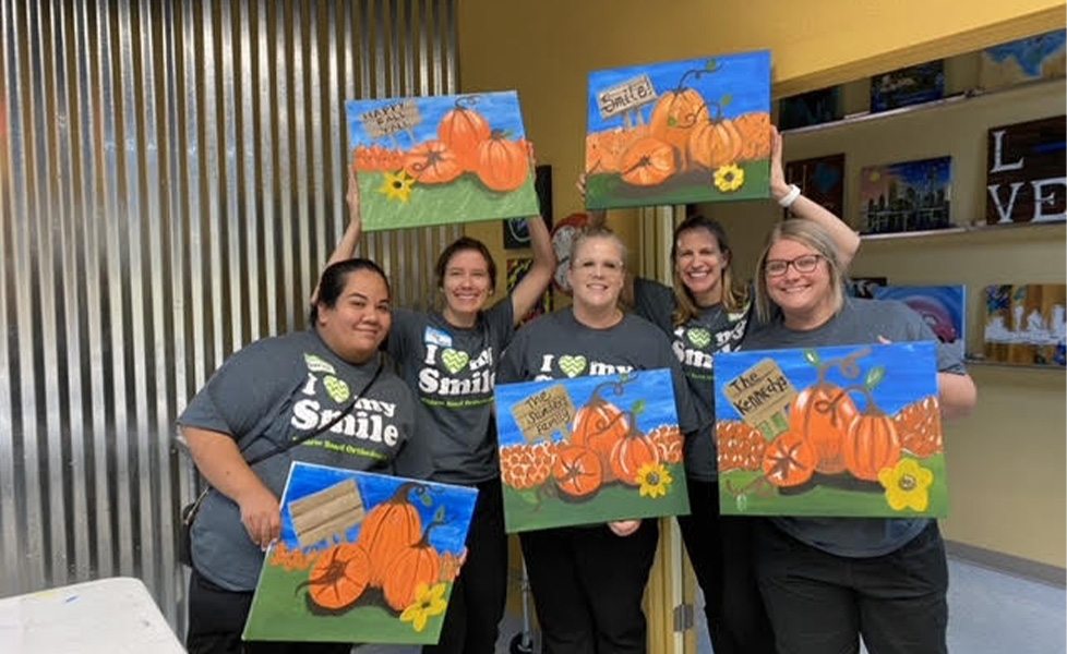 Team members each holding their own painting of pumpkins