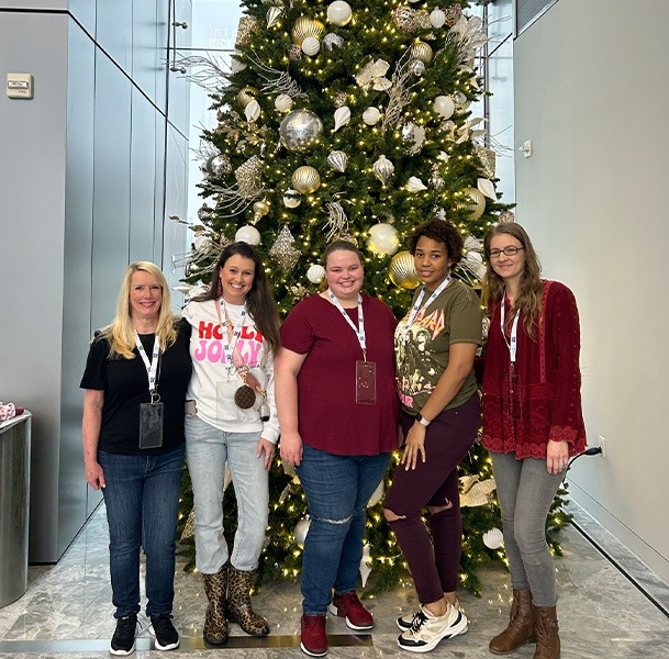 Five young women smiling in front of Christmas tree