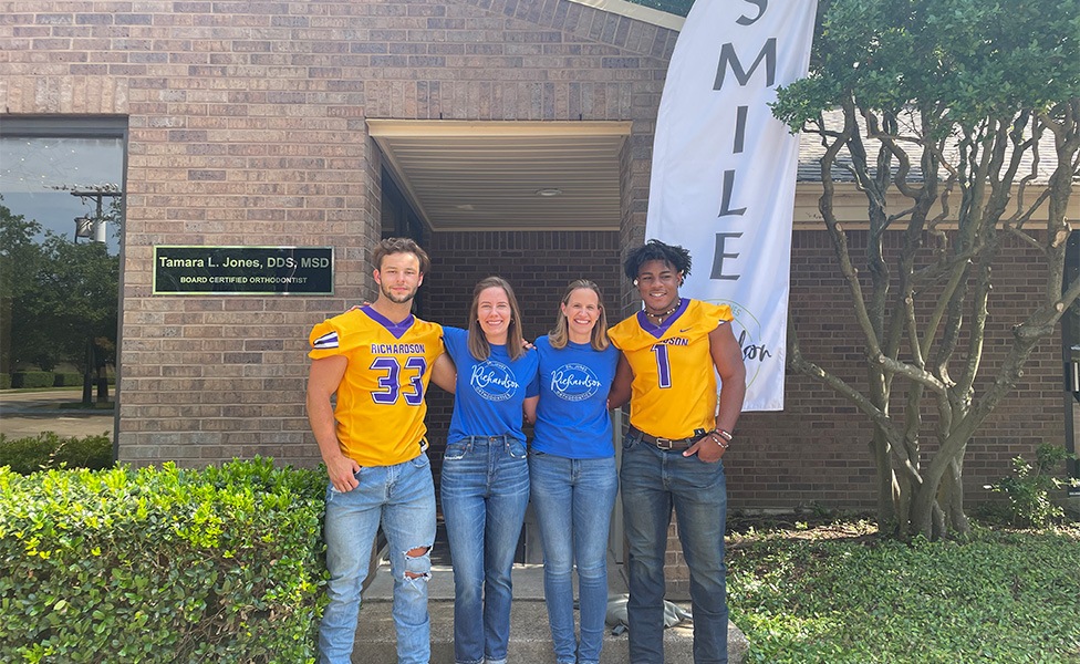 Two women smiling with two young men in football jerseys