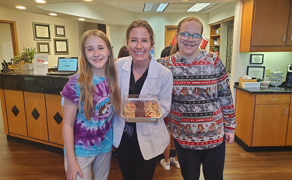 Doctor Hanson holding a box of pastries with two teenage girls in her office