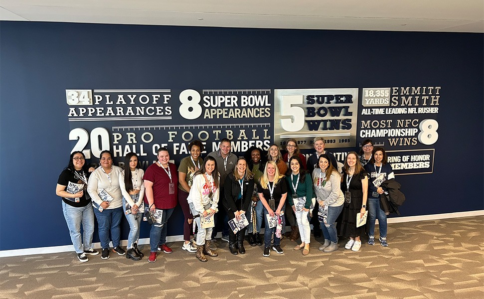 Orthodontic team posing in front of a wall listing the Dallas Cowboys achievements