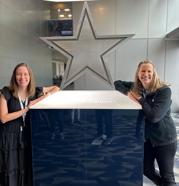 Two women smiling in front of a statue of a Dallas Cowboys star