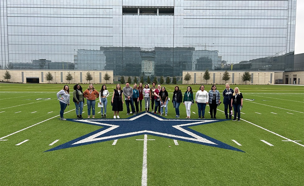 Team members posing on blue star on Dallas Cowboys football field