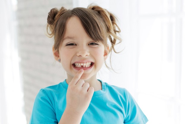 young child with a missing tooth pointing to their smile