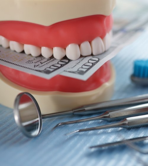 Fake set of teeth holding hundred dollar bills next to dental instruments