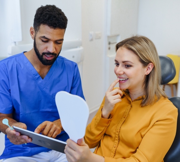 Young woman in dental chair looking at her new smile in a mirror