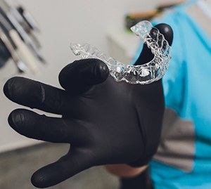 Orthodontist with black glove holding an Invisalign aligner in Allen