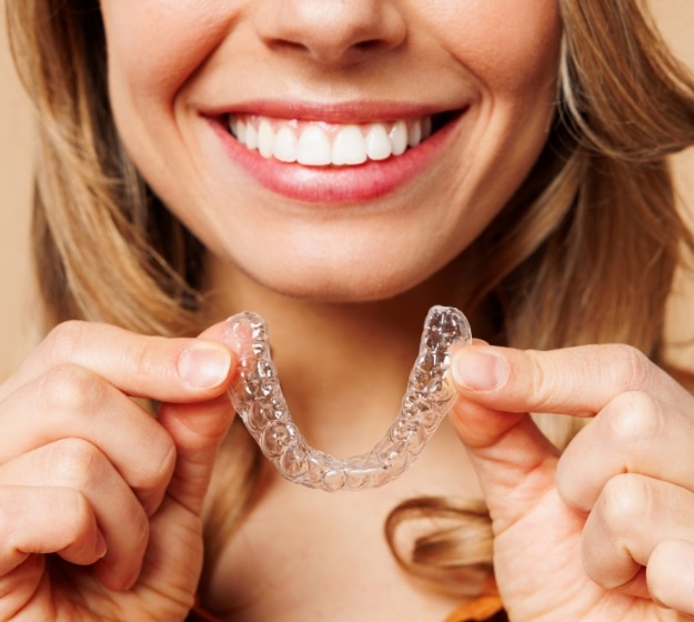 Young woman placing Invisalign Teen aligner over her teeth