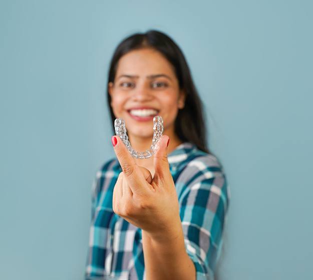 Smiling woman holding a clear aligner