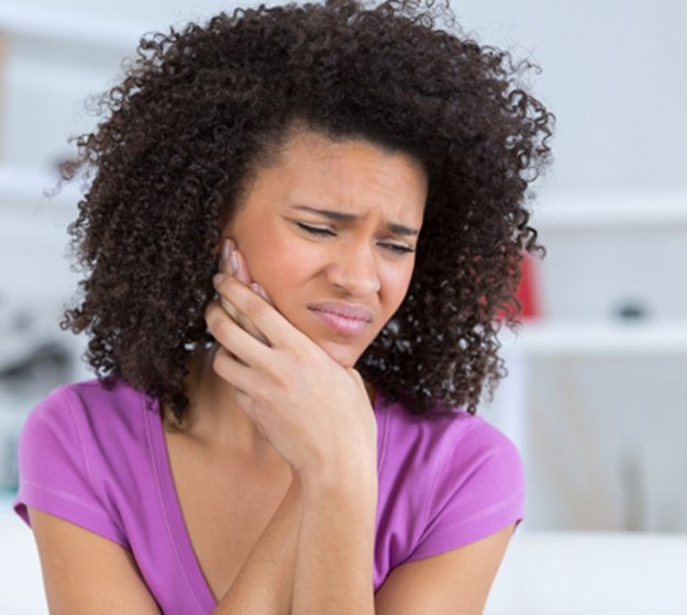 Woman wincing and holding the side of her jaw in pain