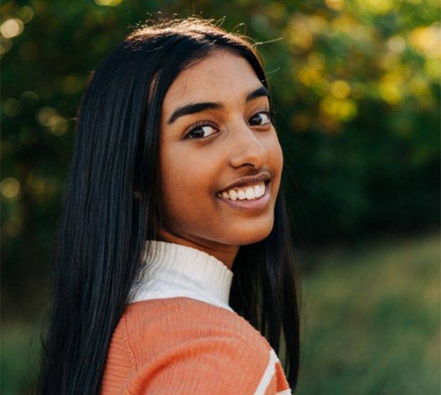 Young woman smiling outdoors with orthodontic retainer in Allen