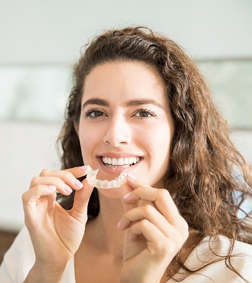 young woman smiling while holding Invisalign clear aligners