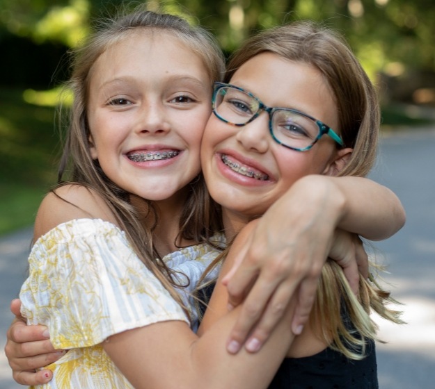 Two young girls with braces hugging and smiling outdoors