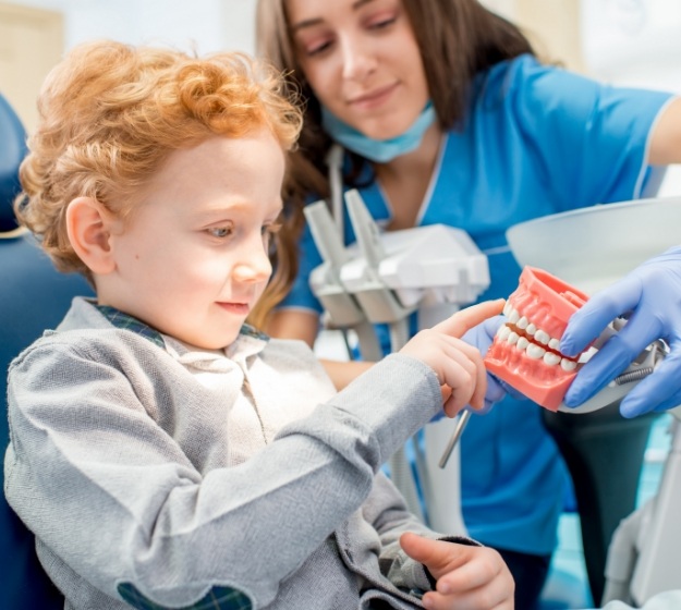 Young boy in dental chair pointing to a model of the teeth